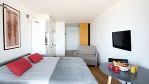 A modern hotel room with a bed, a chair, a TV, and a breakfast table with croissants and juice. - *STUDIO BASIN VIEW*DIRECT ACCESS TO THE BEACH* (Arcachon)