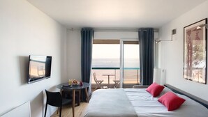 A hotel room with a bed, a desk with a chair, a small table with a chair, and a large window with a view of the sea. - *STUDIO BASIN VIEW*DIRECT ACCESS TO THE BEACH* (Arcachon)