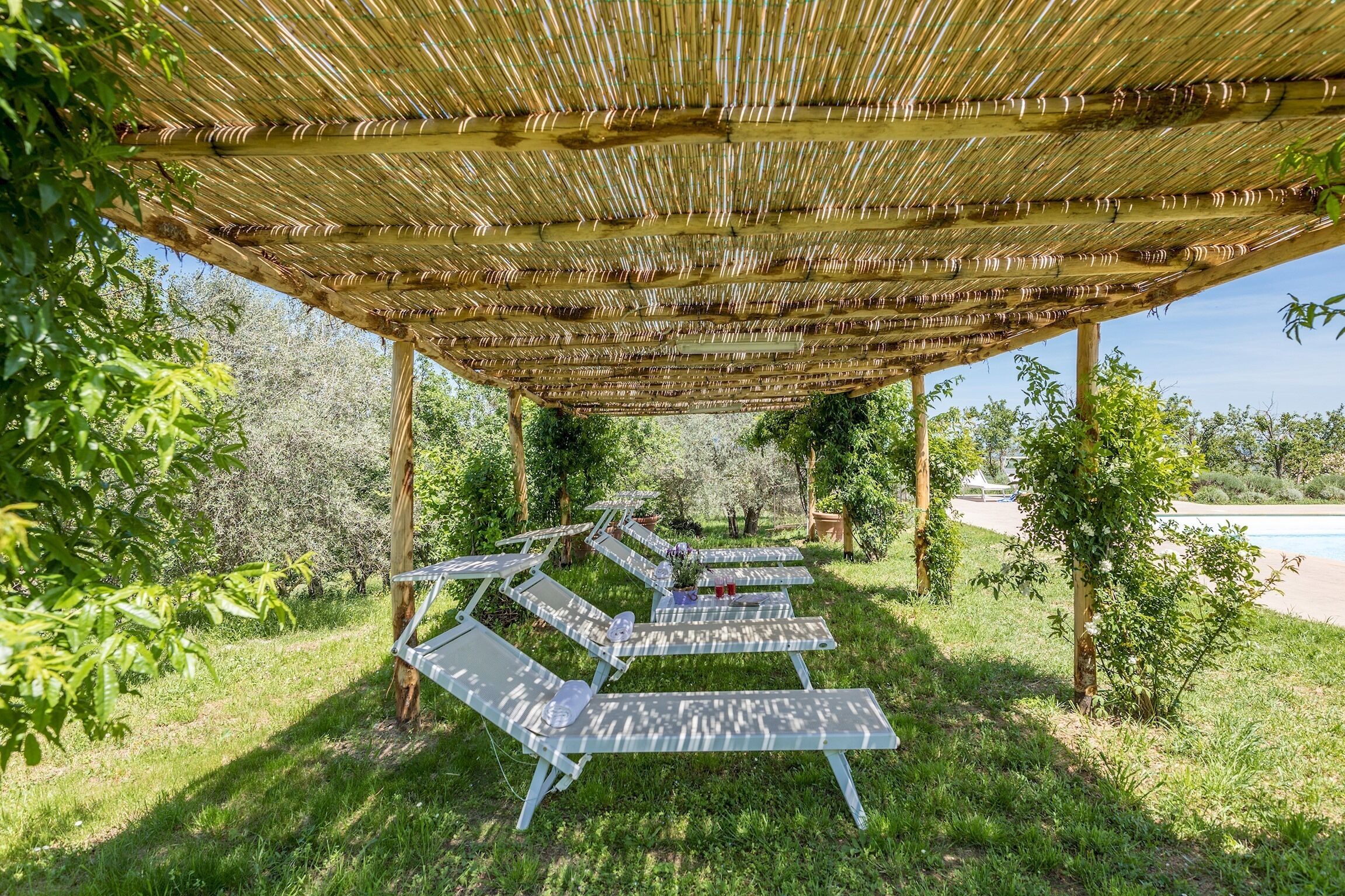 A covered outdoor seating area with lounge chairs and a bamboo roof.