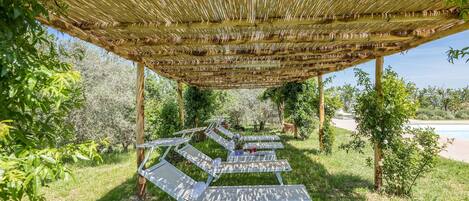 A covered outdoor seating area with lounge chairs and a bamboo roof.