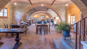A spacious dining area with stone arches, wooden tables, and chairs. - Podere Pratovecchio 14+2, Emma Villas (Montefollonico)