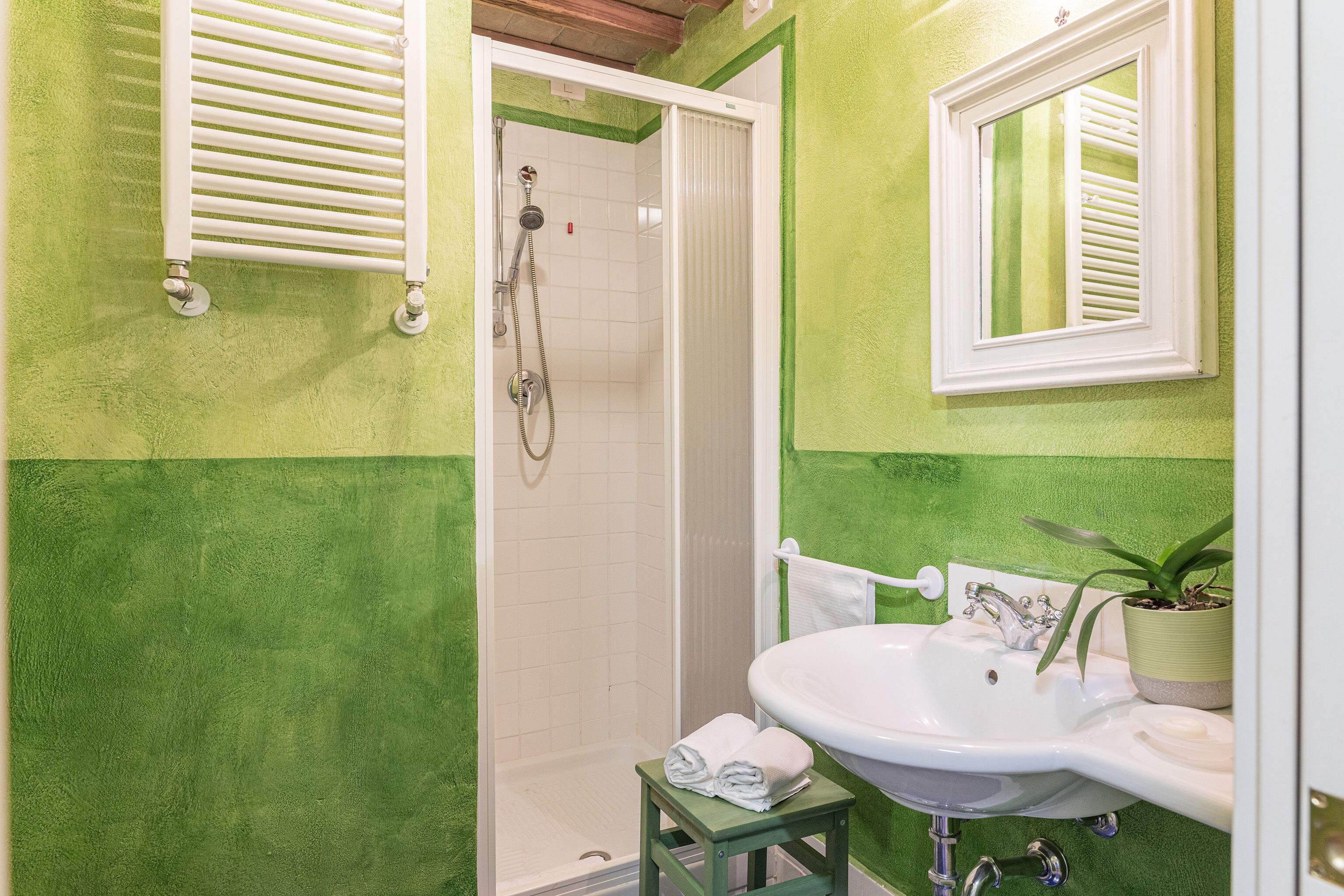 A bathroom with a green wall, a white shower, a sink, and a mirror.