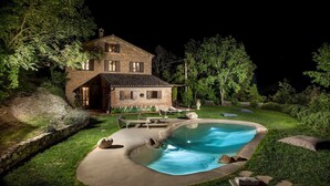 Una casa de dos pisos con piscina, rodeada por un césped cuidado y árboles.