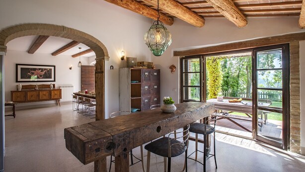Una cocina rústica con barra de madera, arco de piedra y amplios ventanales con vistas a un jardín.
