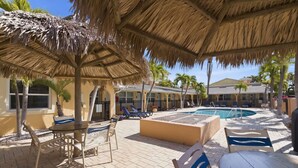 A poolside area with a thatched roof, lounge chairs, and a pool.