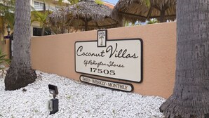 A sign for Coconut Villas with a palm tree and thatched roof structures in the background.