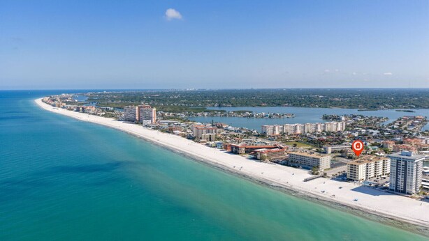 An aerial view of a coastal city with a long sandy beach, high-rise buildings, and a marina.
