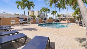 A pool area with lounge chairs, palm trees, and a building in the background.