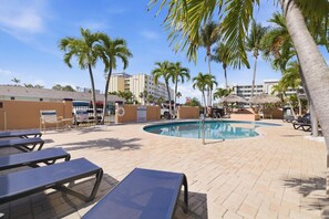 A pool area with lounge chairs, palm trees, and a building in the background.