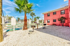 A red building with a gravel patio, a palm tree, and a tennis court in the background.