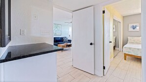 Eine moderne Küche mit schwarzem Arbeitsplatz und weißen Wänden, die in einen Wohnbereich mit Sofa und Couchtisch übergeht.