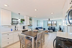 A modern kitchen with white cabinetry, a dining table with chairs, a built-in oven, and a ceiling fan.