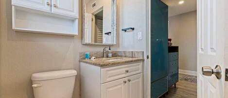 A bathroom with a toilet, a sink with a marble countertop, a mirror above the sink, and a teal cabinet.