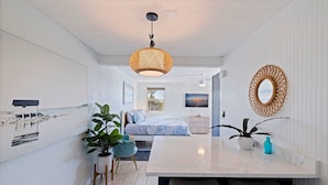 Une chambre moderne avec un grand lit, un luminaire suspendu et une vue sur la plage par la fenêtre.