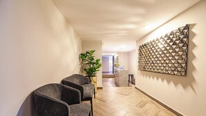 Een gang met drie donkere stoelen, een potplant en een abstract kunstwerk op de muur.
