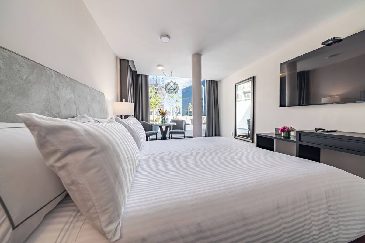 Ein modernes Hotelzimmer mit einem großen Bett, einem Schreibtisch, einem Sessel und einem Fernseher.