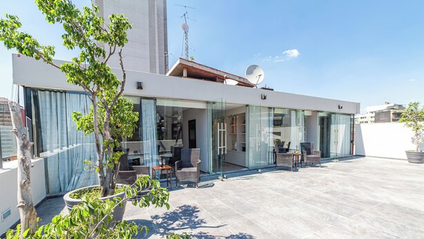 Een modern huis met een glazen gevel, een terras en een schotelantenne.