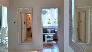 Un interior moderno con un pasillo que conduce a una sala de estar, que incluye un sofá, una mesita y un espejo decorativo.
