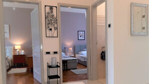 Una habitación de hotel con cama, mesita de noche, lámpara y una pequeña zona de estar con un sillón y un reposapiés.