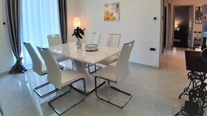 Un comedor moderno con una mesa blanca, cuatro sillas, un jarrón con una planta y un aplique de pared.