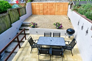 A patio with a table and chairs, a wooden fence, and potted plants. - Just Stay Wales - Hartwell House Mumbles (Swansea)