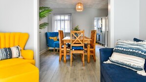 A dining area with a wooden table and chairs, a blue sofa, and a yellow armchair. - Just Stay Wales - Hartwell House Mumbles (Swansea)
