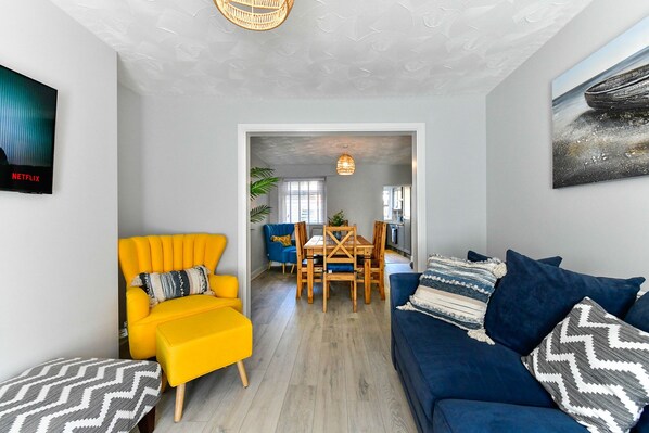 A modern living room with a bright yellow armchair, a blue sofa, and a dining area with wooden furniture. - Just Stay Wales - Hartwell House Mumbles (Swansea)