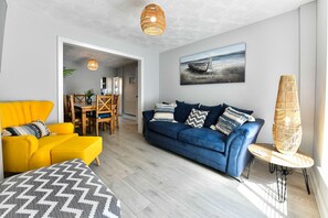 A living room with a yellow sofa, a blue sofa, and a dining area with wooden chairs and a table. - Just Stay Wales - Hartwell House Mumbles (Swansea)