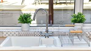 A kitchen sink with a modern faucet, two potted plants, and a dish rack. - Just Stay Wales - Hartwell House Mumbles (Swansea)