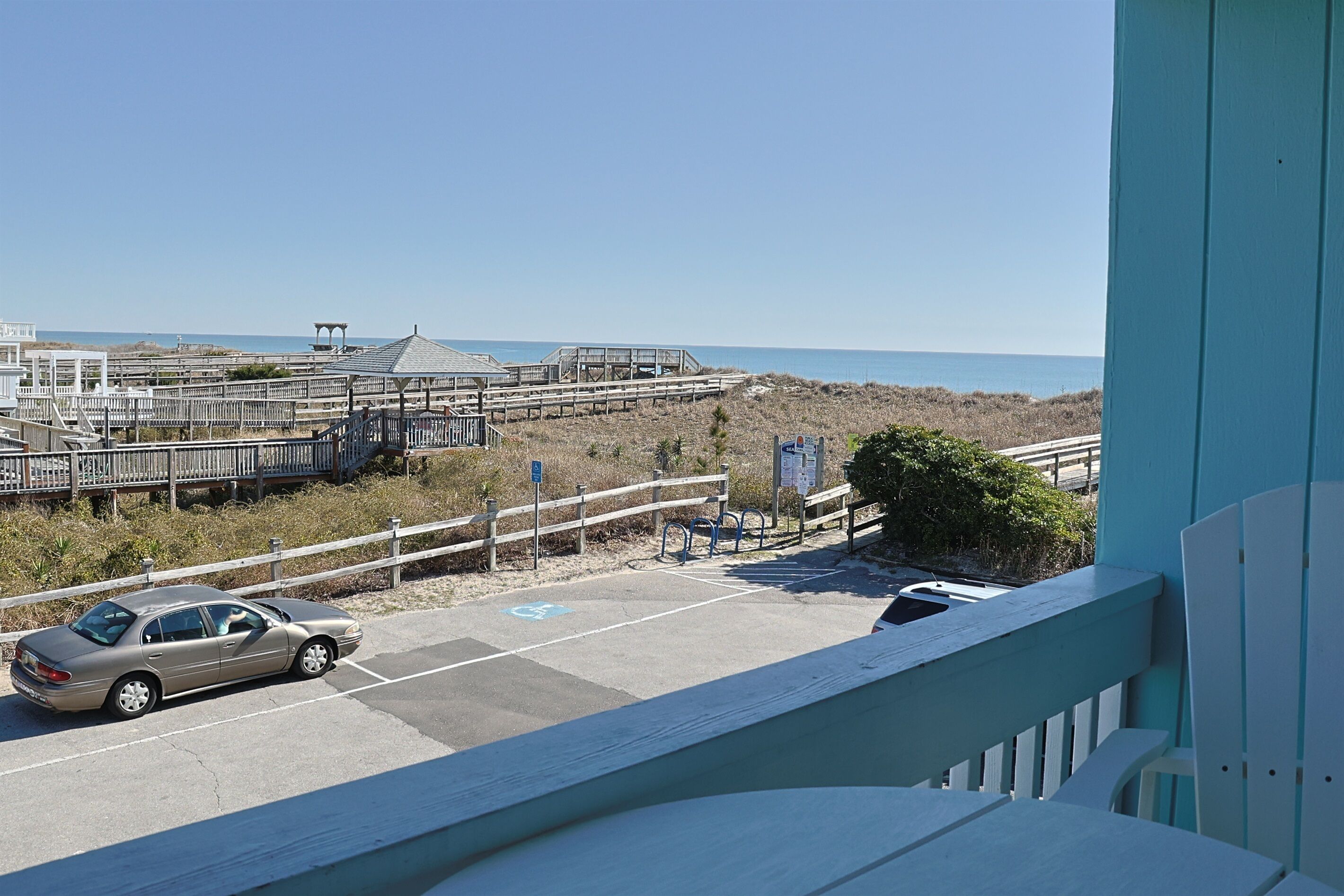 Ein Parkplatz mit einem Auto, einer Fußgängerbrücke und Blick auf Strand und Meer.