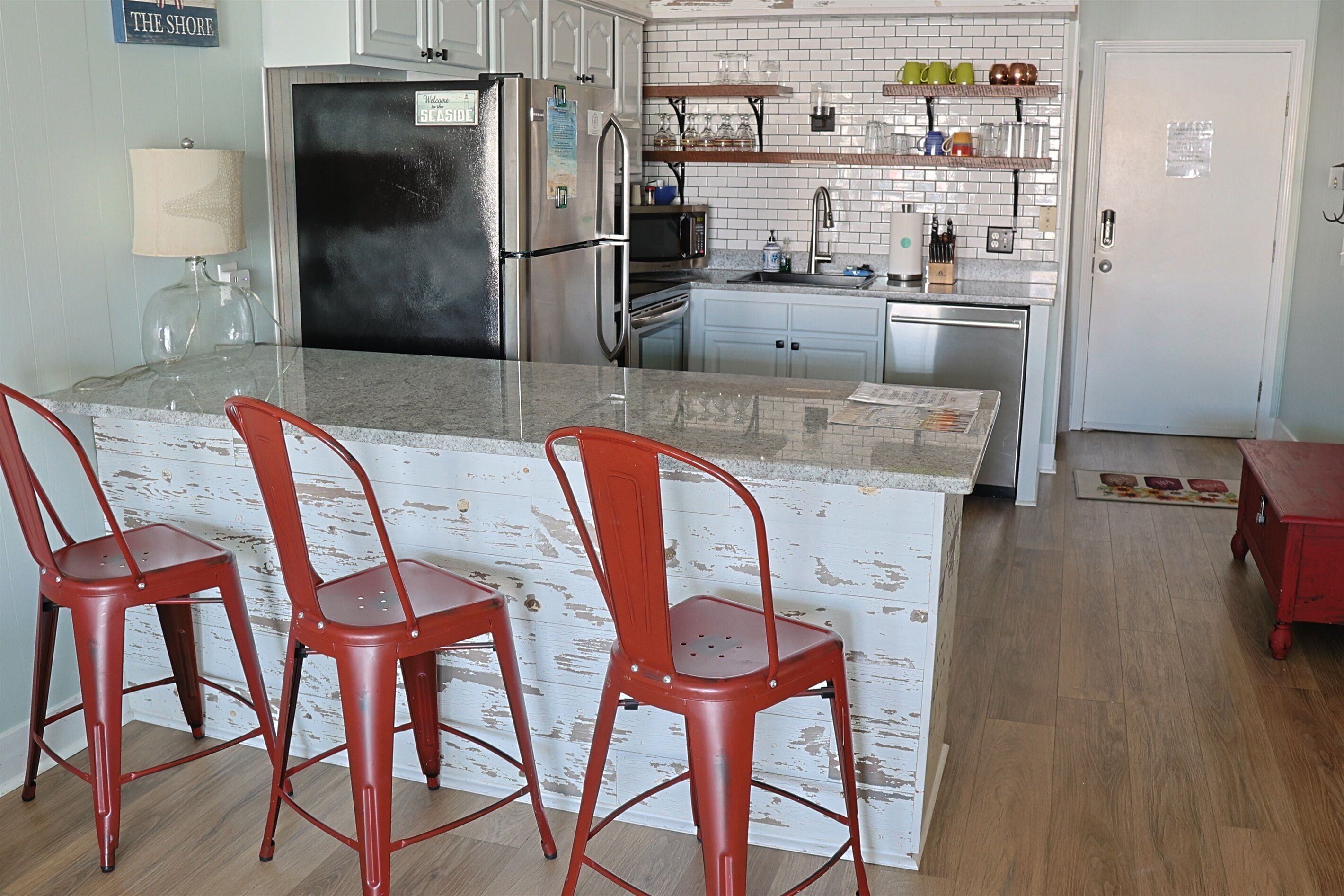 Una cocina con una isla central, taburetes rojos, un refrigerador, un microondas y un lavamanos.