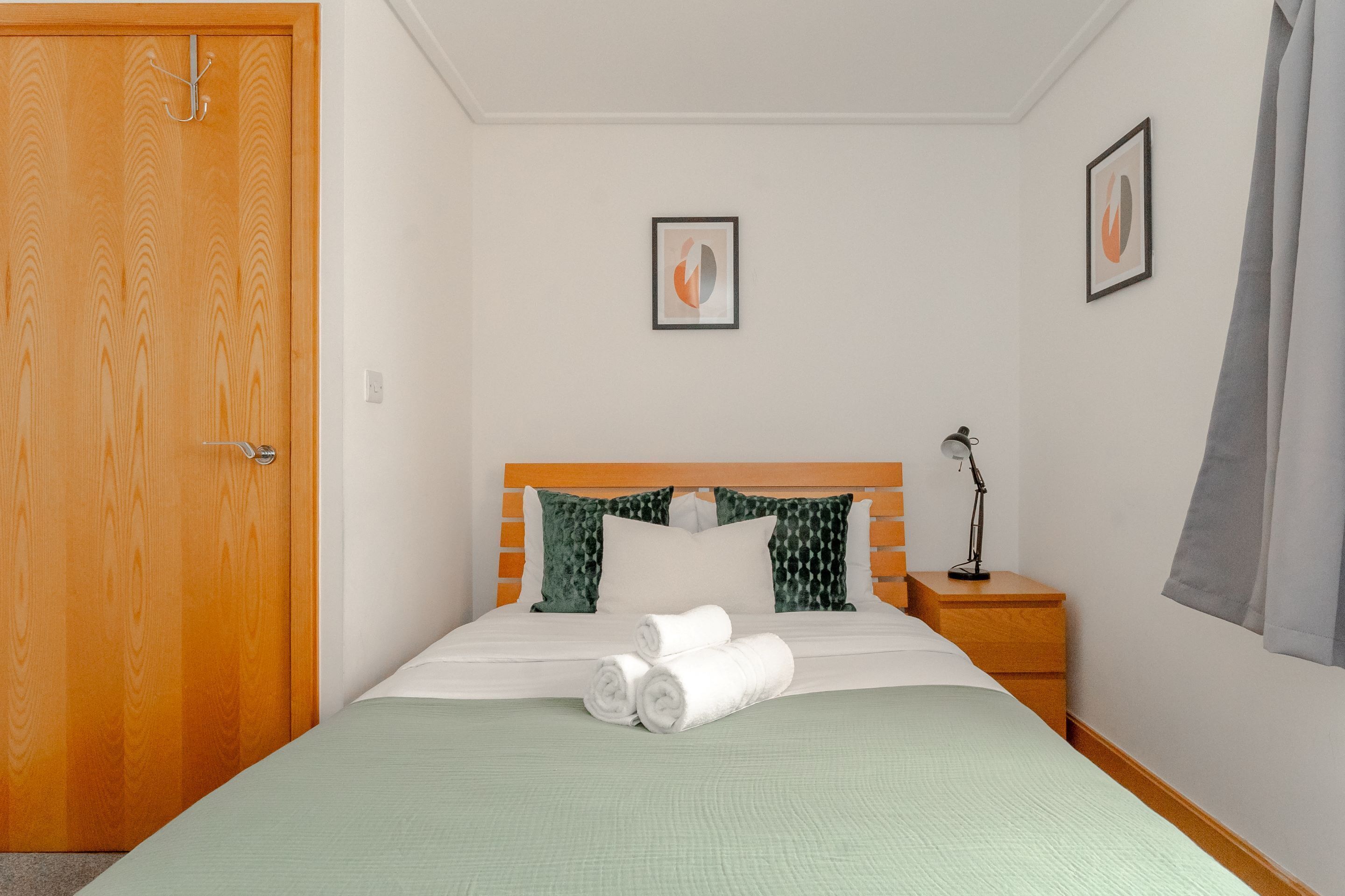 A neatly made bed with rolled white towels, a wooden headboard, and a nightstand with a lamp.