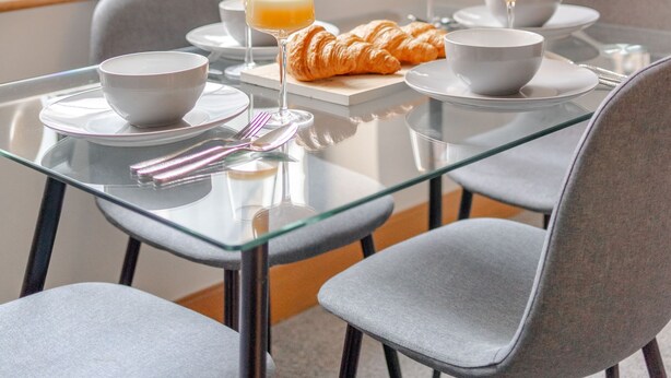 Ein Essbereich mit einem Glastisch, grauen Stühlen und einem Croissant auf einem Teller.