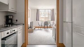 Eine moderne Küche mit weißen Schränken, einem Herd und einer Kaffeemaschine. Es gibt einen Essbereich mit Tisch und Stühlen sowie ein Fenster mit Vorhängen.