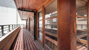 Eine Holzterrasse mit Geländer, großen Fenstern und Blick auf Gebäude im Hintergrund.