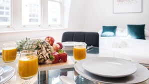 Frühstückstisch mit Obst, Saftgläsern und Tellern in einem Hotelzimmer, im Hintergrund ein Bett mit Kissen.