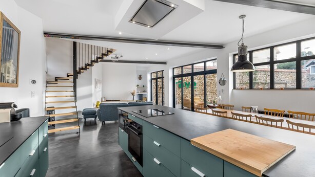 A modern kitchen with a central island, a staircase, and large windows.