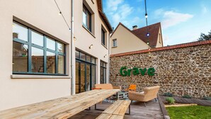 An outdoor seating area with wooden benches and chairs, a stone wall with the word "Grage" on it, and a clear sky.