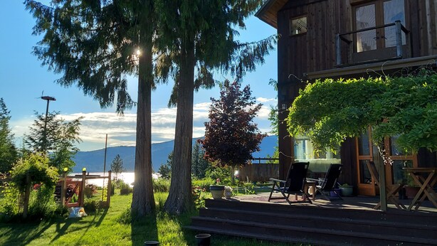 A wooden cabin with a deck, surrounded by trees and a view of mountains. - Your Lake & Mountain vacation awaits... (Sagle)