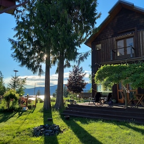 A wooden cabin with a deck, surrounded by trees and a view of mountains. - Your Lake & Mountain vacation awaits... (Sagle)