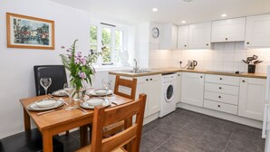 Una cocina moderna con armarios blancos, una mesa de comedor con sillas, una lavadora y un reloj en la pared.