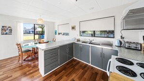 Una cocina moderna con una isla central, armarios grises oscuros, una estufa blanca y un ventanal con vistas a un jardín trasero.