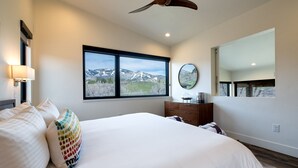 Ein Schlafzimmer mit einem großen Bett, einem Schminktisch, einem Spiegel und einem Fenster mit Blick auf die Berge.
