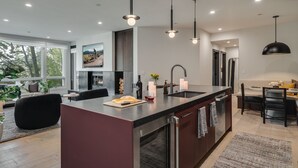 Een moderne keuken met een centraal kookeiland, roestvrijstalen apparatuur en hanglampen.