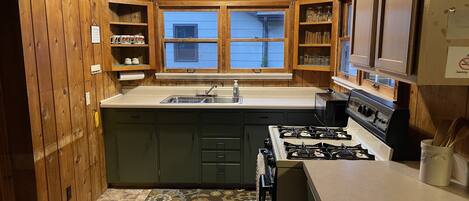 A kitchen with wooden cabinets, a gas stove, a sink, and a window with a view.