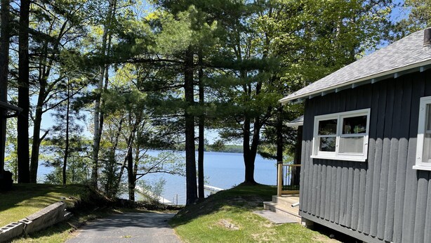 A cabin with a gravel path leading to a dock by a lake, surrounded by trees. - Spacious, three bedroom cottage on beautiful Lake Metonga. (Crandon)