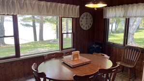 A wooden dining room with a round table, chairs, a clock, and large windows with curtains. - Spacious, three bedroom cottage on beautiful Lake Metonga. (Crandon)
