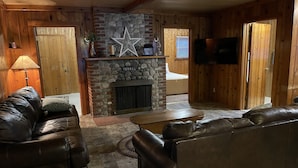A cozy living room with a stone fireplace, leather sofas, and a television mounted on the wall. - Spacious, three bedroom cottage on beautiful Lake Metonga. (Crandon)