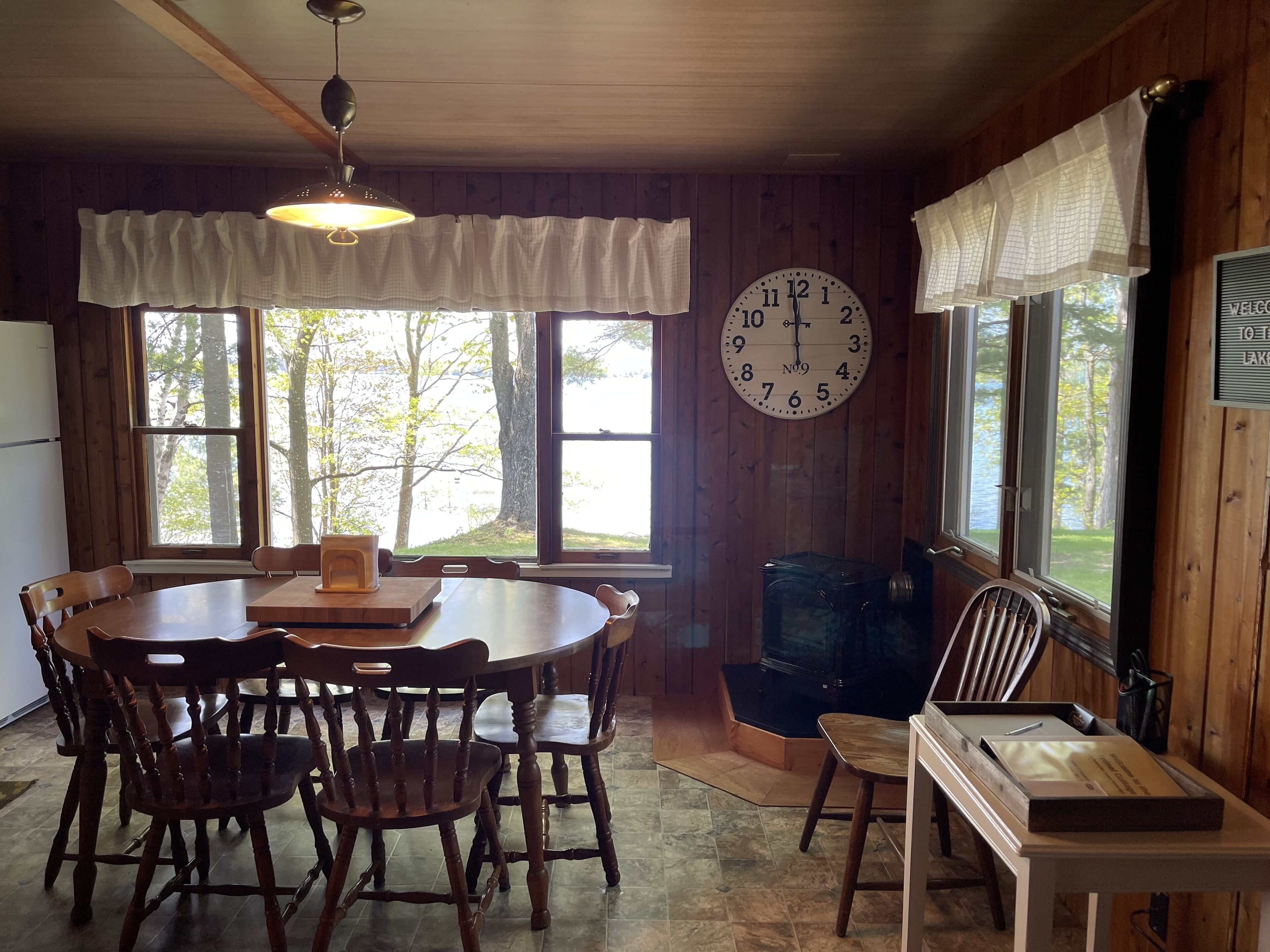 Un coin repas aménagé dans une cabane en bois, avec une table ronde, des chaises, une horloge et une cheminée.