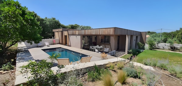 Une maison moderne dotée d’une piscine, d’un espace salon extérieur et d’un jardin.
